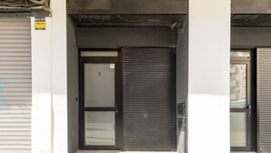 A closed storefront with a metal shutter door and a glass door, a metal sign on the wall, and a tiled pavement. - Travel Habitat Nou Mestalla 1 (Valencia)