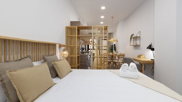 A modern hotel room with a large bed, a wooden headboard, a desk with a chair, a small table, and a hanging light fixture. - Travel Habitat Nou Mestalla 1 (Valencia)
