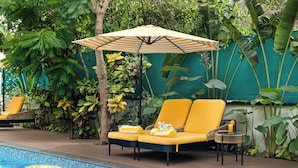 A poolside area with a lounge chair, an umbrella, and a small table with a drink. - Saligao - Casa De Mello C 1863 (Saligao)