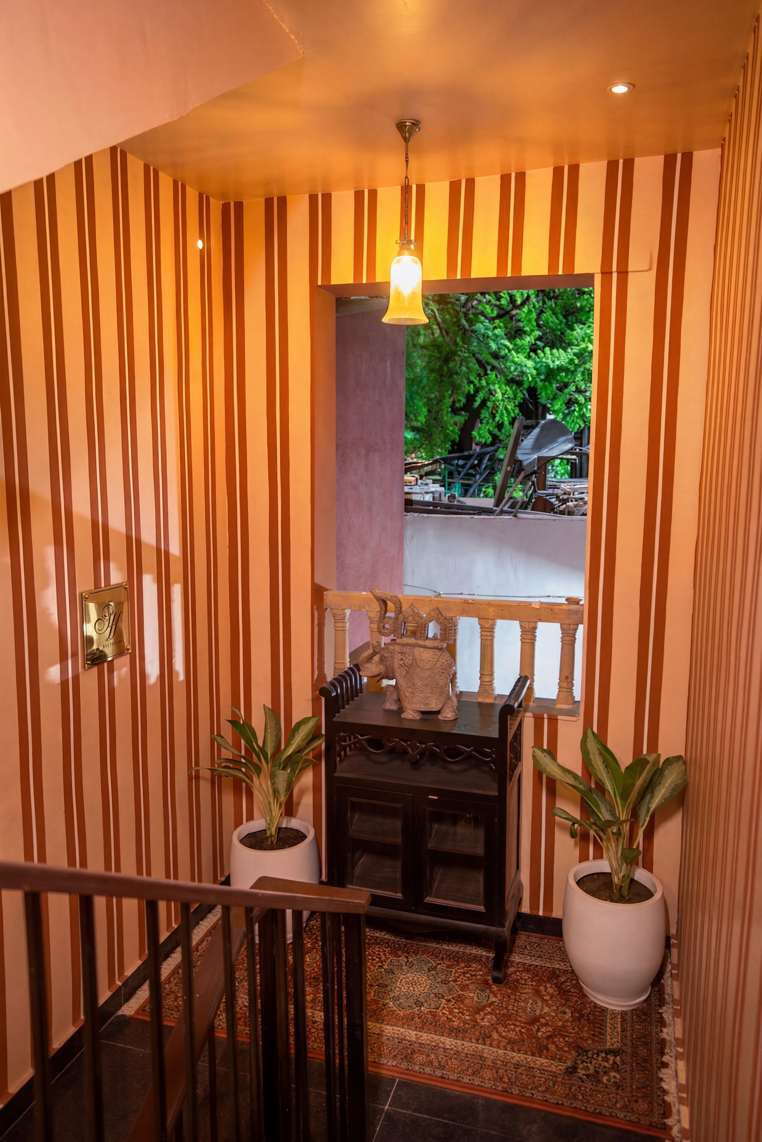 A staircase with striped walls, a wooden railing, and two potted plants.