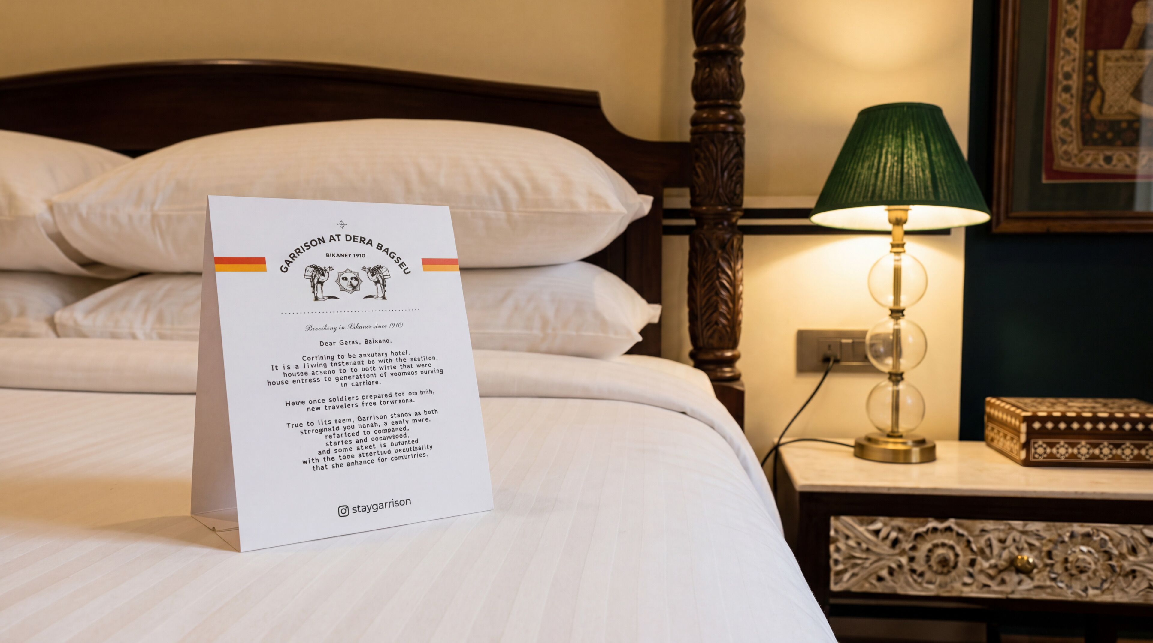 Una habitación de hotel con cama, almohadas, una mesita de noche con lámpara y un cuadro en la pared.
