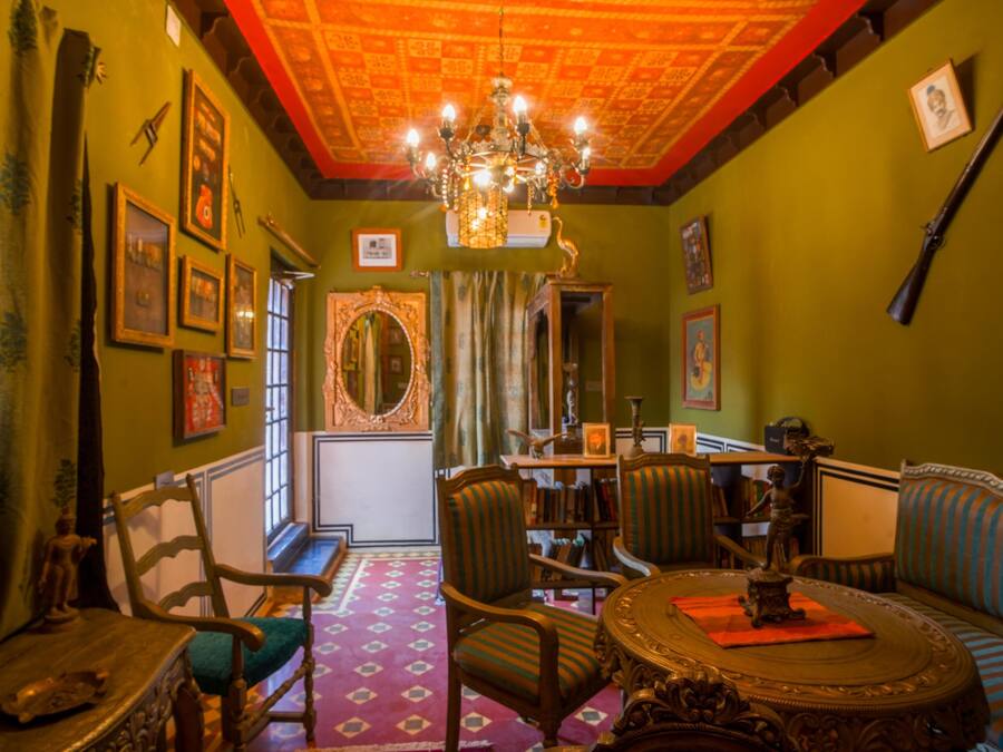 Una habitación con candelabro, paredes verdes, un espejo y un sofá.