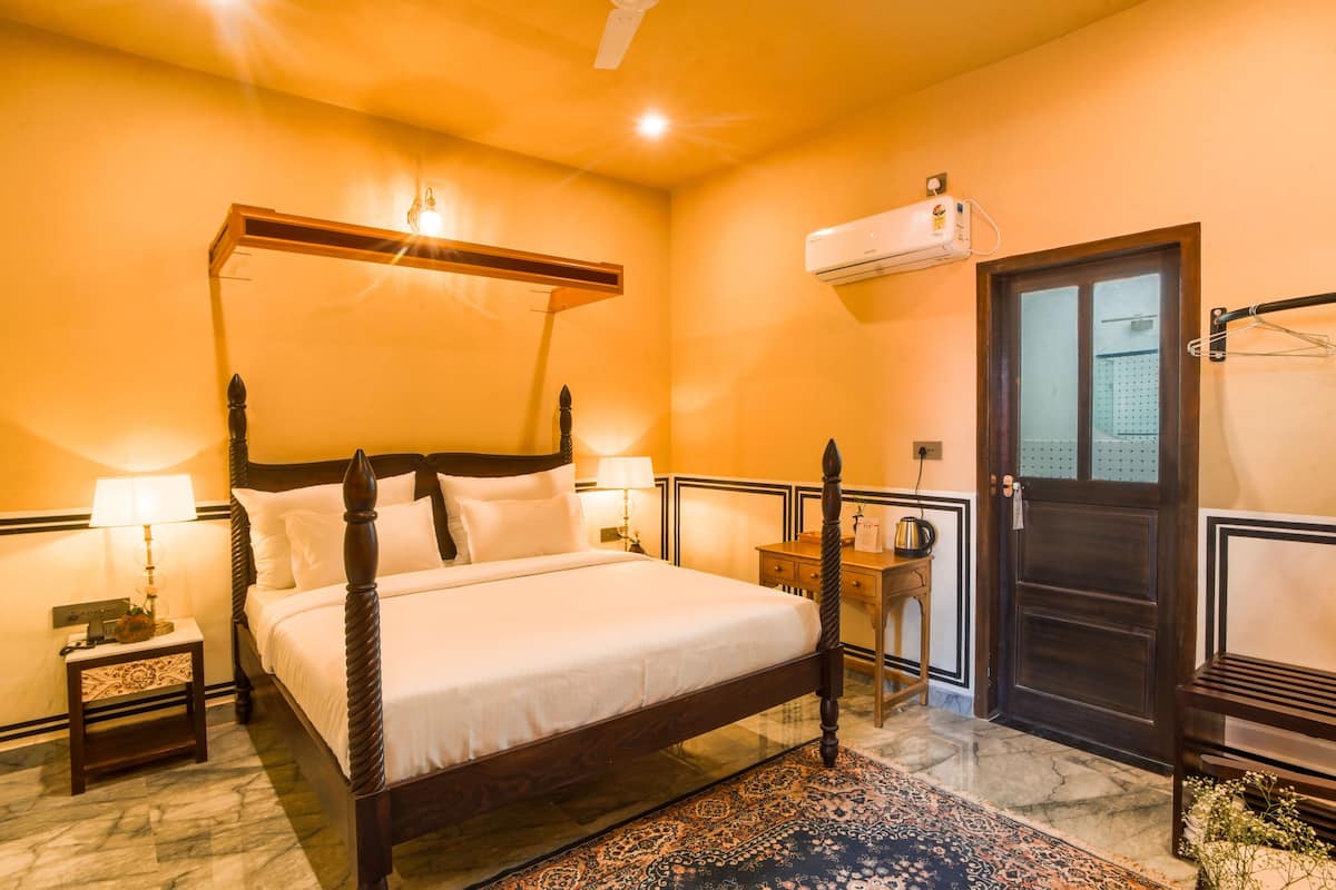 Une chambre d’hôtel avec un lit à baldaquin, un sol en marbre, une table de chevet en bois, un bureau et une armoire.