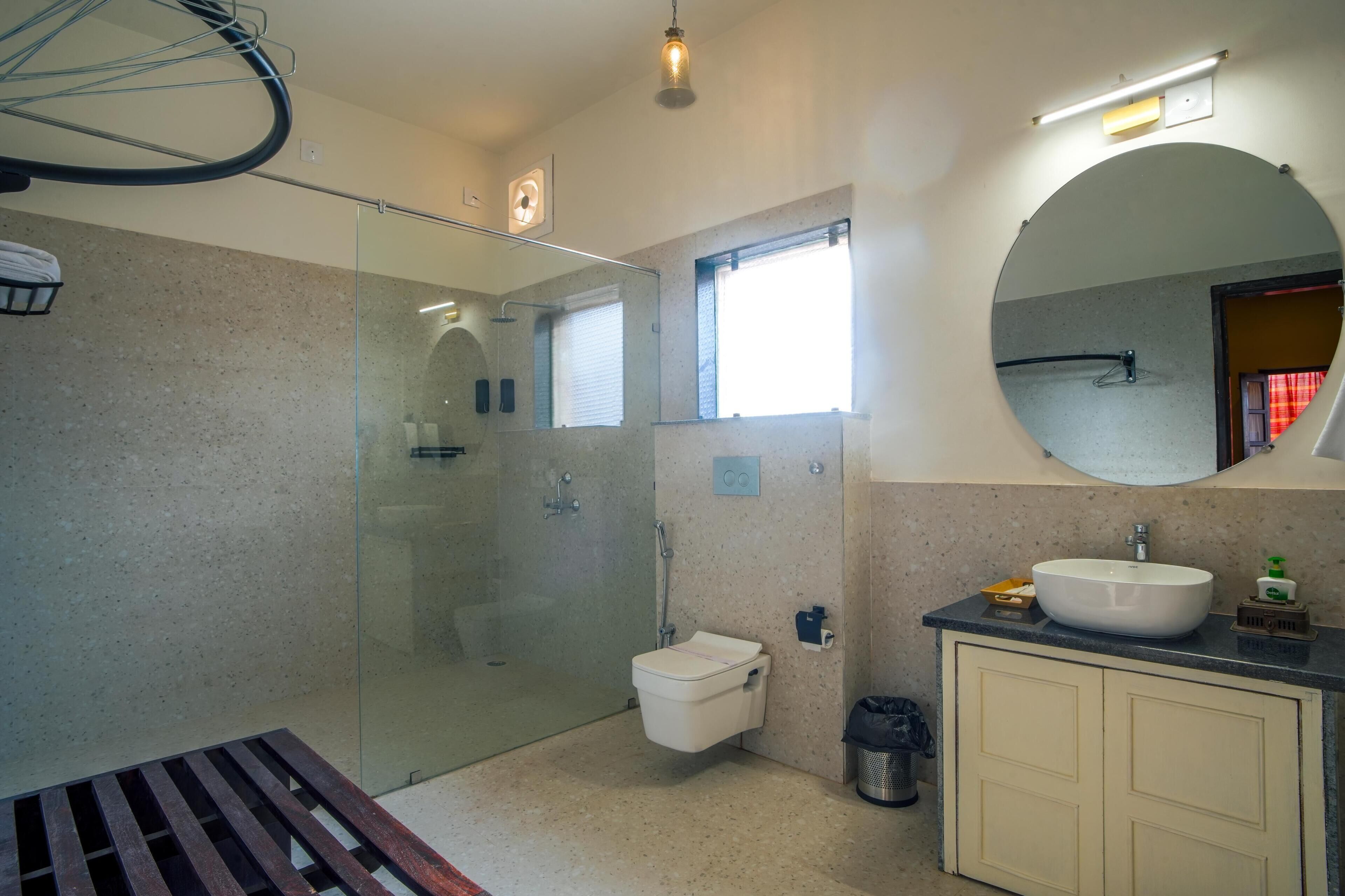 Un baño con cabina de ducha de vidrio, inodoro, lavamanos con espejo y un pequeño cubo de basura.