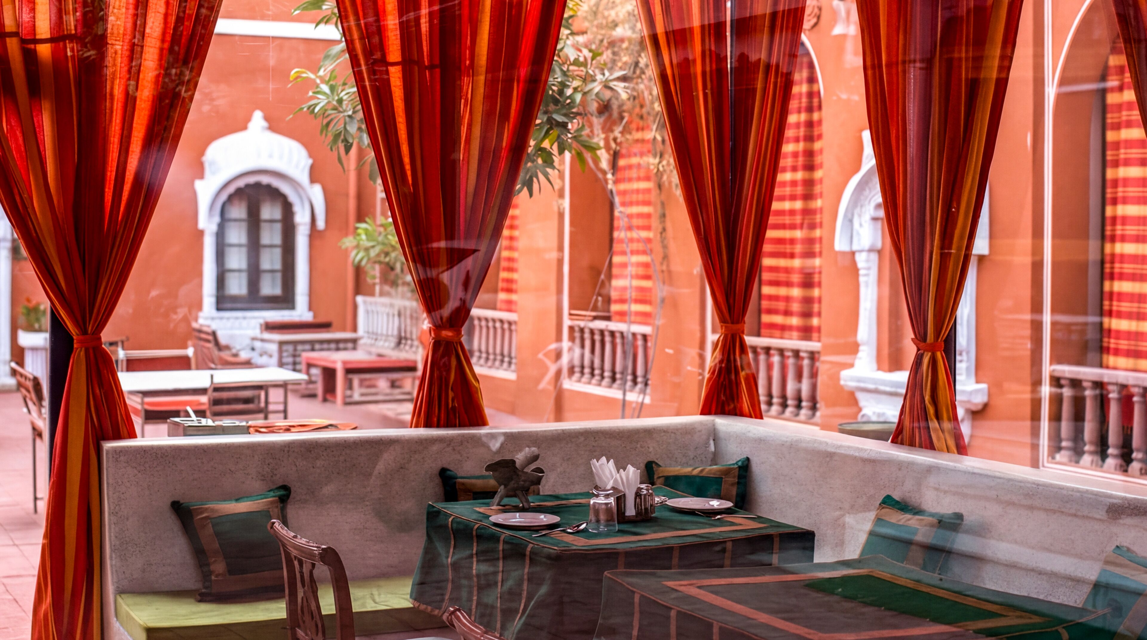 An outdoor seating area with tables and chairs, red curtains, and a view of a building with arches.