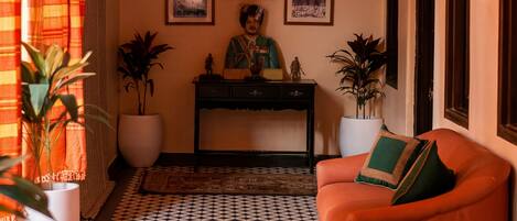 A room with a patterned floor, a sofa, a desk with a statue, and framed pictures on the wall.