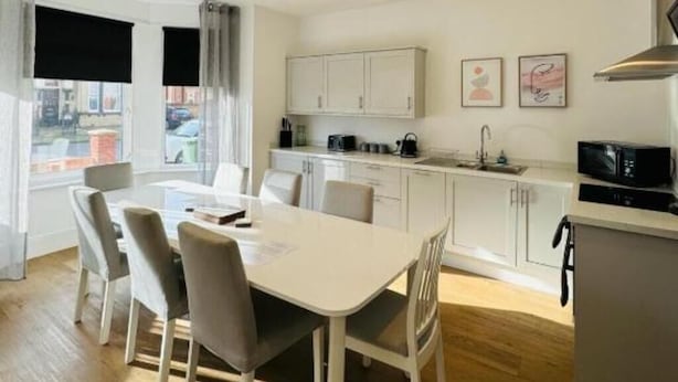 Una cocina moderna con armarios blancos, una mesa de comedor con sillas y un microondas.