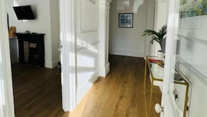 Un pasillo con suelo de madera, paredes blancas y un arco de entrada a otra habitación.