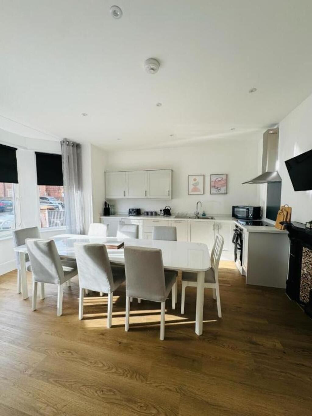 Una cocina moderna con armarios blancos, un comedor con una mesa y sillas blancas, y una chimenea.