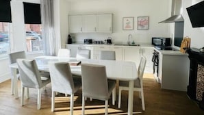Una cocina moderna con armarios blancos, un comedor con una mesa y sillas blancas, y una chimenea.