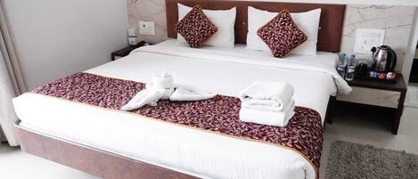 A hotel room with a large bed, two pillows, a nightstand with a kettle, and a water bottle.