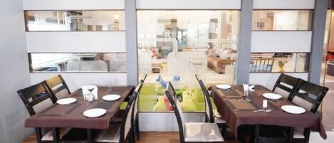 Un espace repas avec vue à travers une paroi de verre, comprenant une table dressée pour quatre personnes avec des chaises, un plancher en bois et une cuisine visible en arrière-plan.