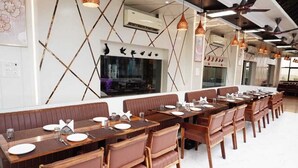 A restaurant with long wooden tables and brown leather booths, arranged in a linear fashion. - BULDHANA URBAN RESIDENCY CLUB (Buldana)