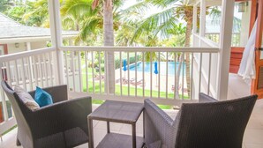 A covered outdoor area with wicker furniture and a view of a pool and palm trees. - Spacious ocean view king bed villa 2 minutes from the restaurant pool and beach (FreeTownst)