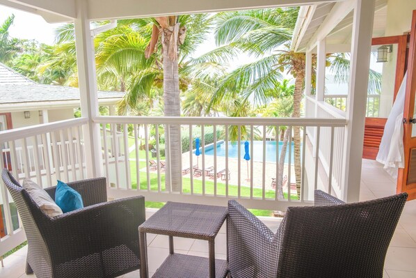 A covered outdoor area with wicker furniture and a view of a pool and palm trees.