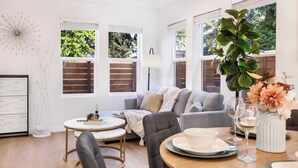 Een moderne woonkamer met een grijze bank, een ronde salontafel en een eettafel gedekt voor twee personen.