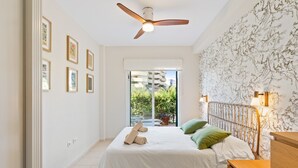 Un dormitorio con cama, ventilador de techo, mesita de noche y vistas al exterior.