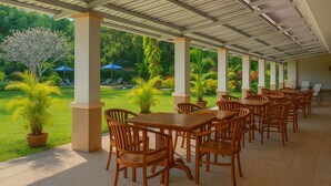 A covered outdoor seating area with wooden tables and chairs, surrounded by greenery and a view of a well-maintained lawn. - 5 Star Resort Patong Beach - Olympic Size Pool, Gym (Patong)