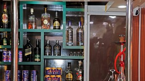 Zona de bar con estantes llenos de botellas de licor y latas, un narguilé y una barra metálica.