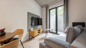 Een moderne woonkamer met een bank, een aan de muur bevestigde televisie, een houten eettafel en een bijzettafeltje.