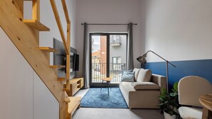 Een moderne woonkamer met een houten trap, een bank, een salontafel en uitzicht door een grote schuindeur.