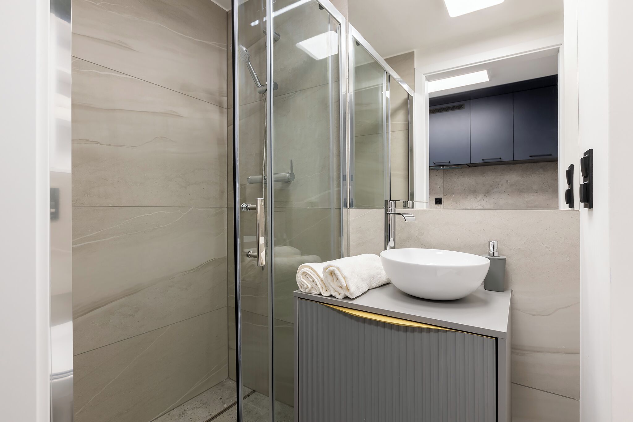 Un baño moderno con cabina de ducha de vidrio, lavamanos blanco con recipiente y una toalla sobre la encimera.