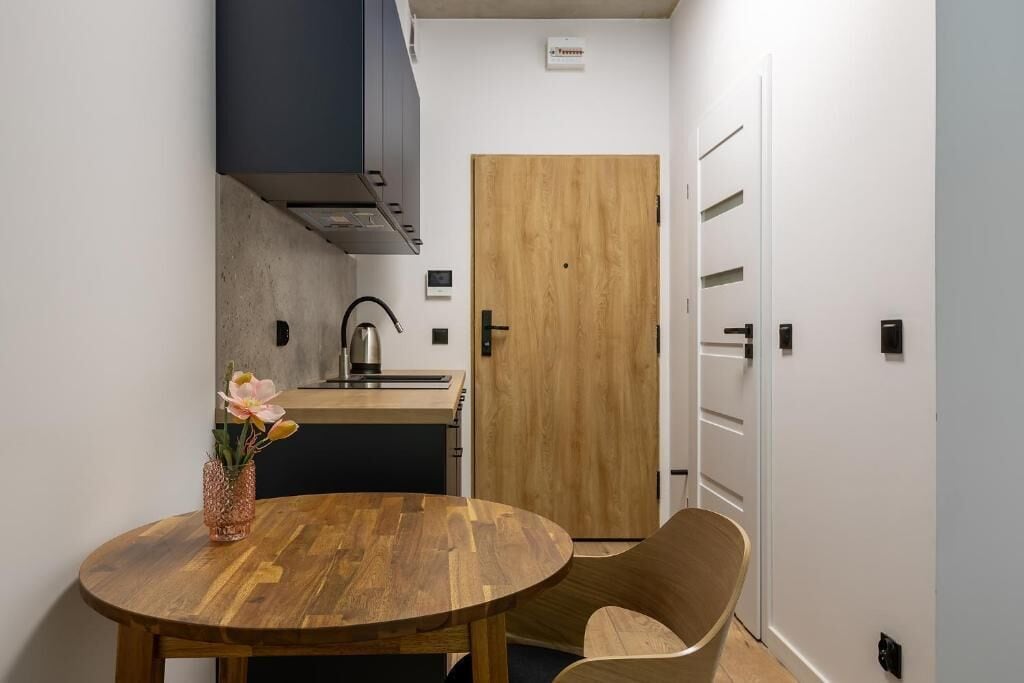 A compact kitchen with a wooden table, a chair, and a vase with flowers.