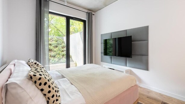 Een moderne slaapkamer met een bed, een aan de muur bevestigde televisie en een groot raam met gordijnen.