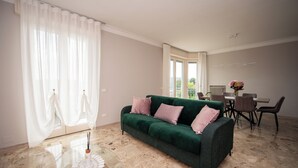 A spacious living room with a green sofa, a glass coffee table, and a dining area with chairs and a table. - Sogni di Lago (Salò)