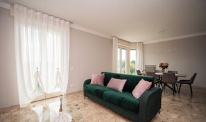 Un salon spacieux avec un canap é vert, une table basse en verre et un coin repas comprenant des chaises et une table.