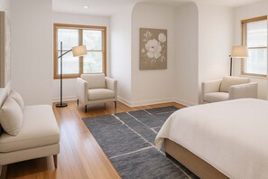 A hotel room with a bed, two armchairs, a floor lamp, and a painting on the wall.