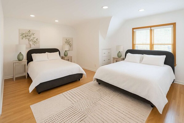 A bedroom with two beds, wooden flooring, and a large window with blinds. - The Hillside - Historic Tudor retreat in SLC (Salt Lake City)