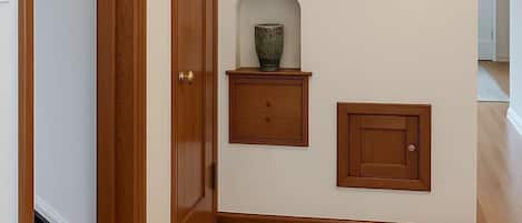 A hallway with wooden flooring, a leopard print bench, a decorative wall piece, and two wooden cabinets.
