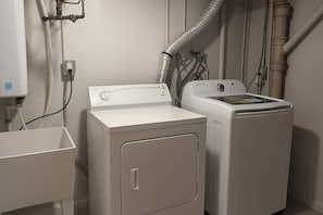 Een wasruimte met een voorlader wasmachine en droger, een spoelbak en zichtbare leidingen.