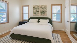 Un dormitorio con cama, mesita de noche, un cuadro y una puerta.