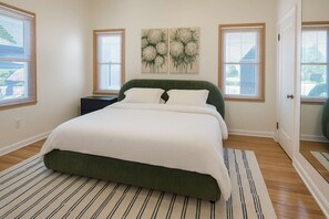Een slaapkamer met een bed, nachtkastje, schilderij en een deur.
