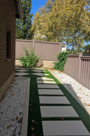 Un sentier bordé de pierres plates qui mène à une zone délimitée par une grille, où se trouvent des arbres et une clôture.