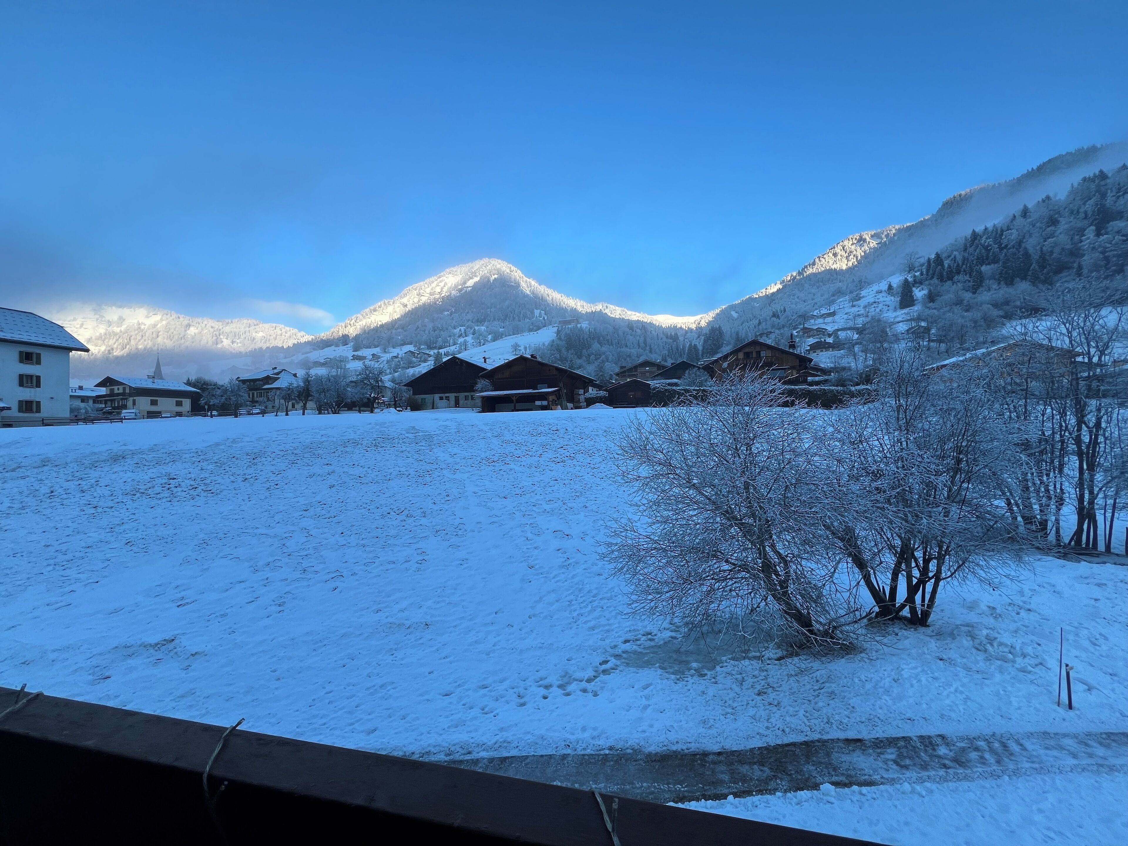 Schneeverdeckte Landschaft mit Gebäuden und Bergen im Hintergrund.