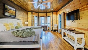 Een slaapkamer in een houten hutje, met een bed, een bureau en een televisie.