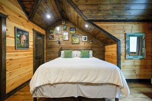 A wooden cabin bedroom with a bed, framed pictures on the walls, and a window.