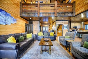 A spacious living area with a wooden ceiling, a sofa set, a coffee table, and a kitchen area in the background.