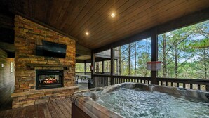 Een houten terras met een stenen open haard, een jacuzzi en een televisiescherm.