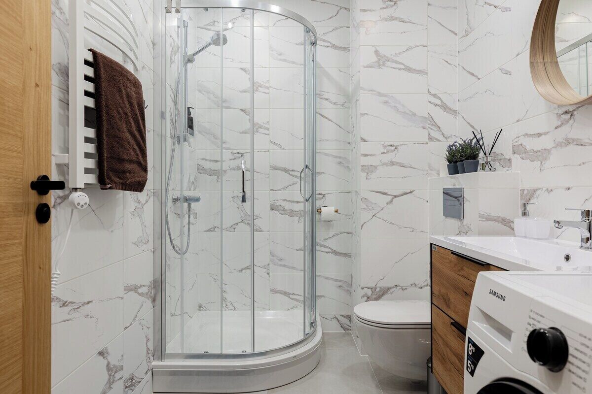 Un baño moderno con ducha de vidrio, inodoro y lavadora Samsung.