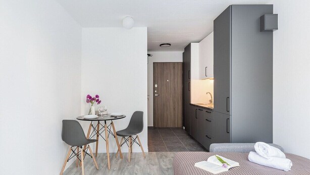 Une chambre d’hôtel moderne comprenant un lit, une petite table à manger avec des chaises, un coin cuisine et une salle de bain visible à travers une porte ouverte.