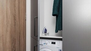 A compact, modern laundry room with a built-in washer and dryer, a small ironing board, and a towel hanging on the wall. - River to the City Self check in (Vilnius)