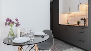 A modern kitchen with grey cabinets, a black dining table, and a vase of flowers. - River to the City Self check in (Vilnius)