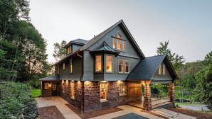 A large, two-story house with a stone facade and a dark roof, surrounded by lush greenery.