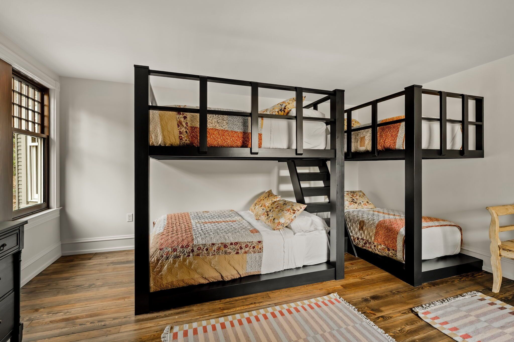 Une chambre avec un lit superposé, un plancher en bois, une fenêtre et une chaise.
