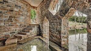 A stone staircase leading to a pond, surrounded by stone walls and a wooden ceiling.