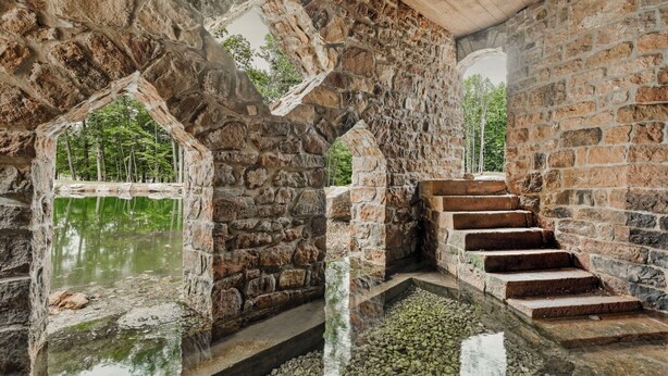 A stone interior with a reflective water feature and a staircase.